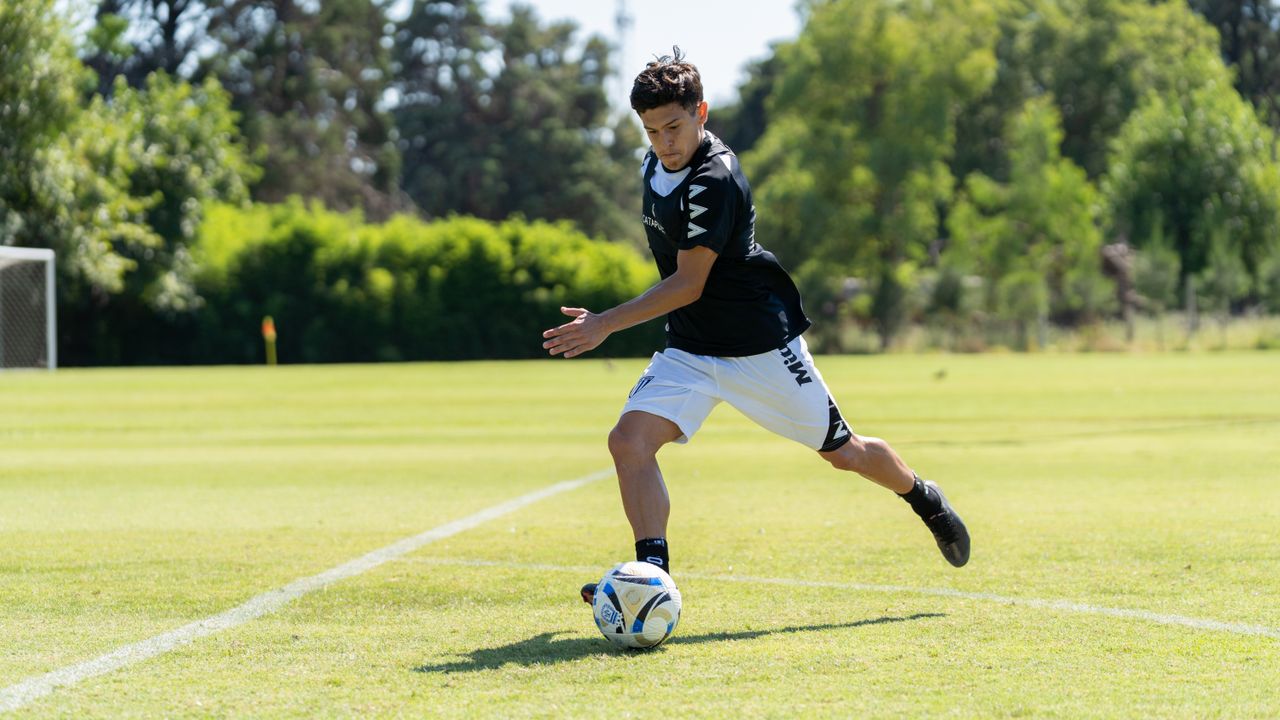 A teenager playing soccer on a sunny day, dribbling the ball on a grassy field.